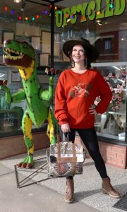 Girl outside a store with a hat and a bag with an inflatable dinosaur outside the store